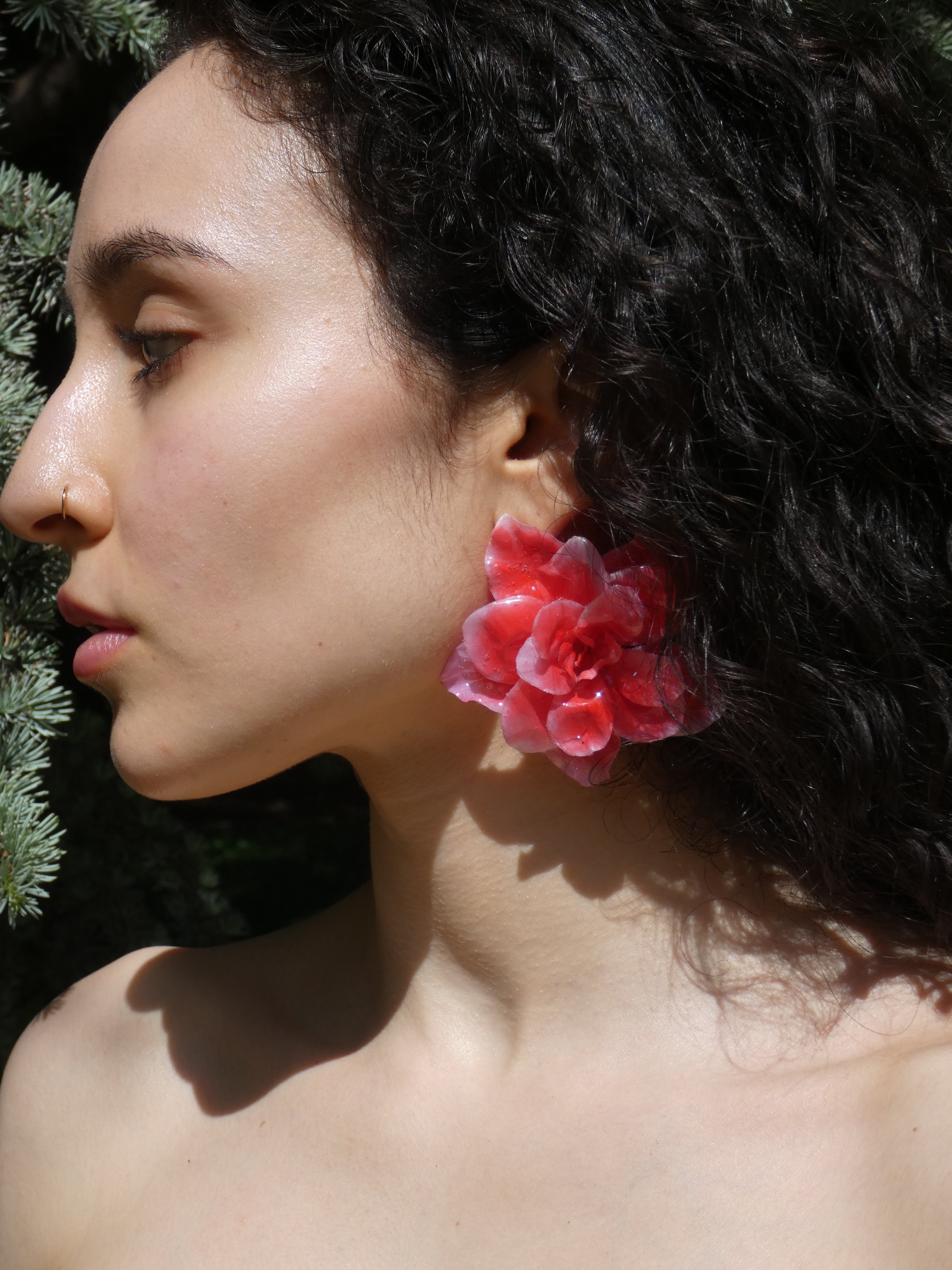 Détail d’une boucle d’oreille fleur rouge corail aux pétales texturés