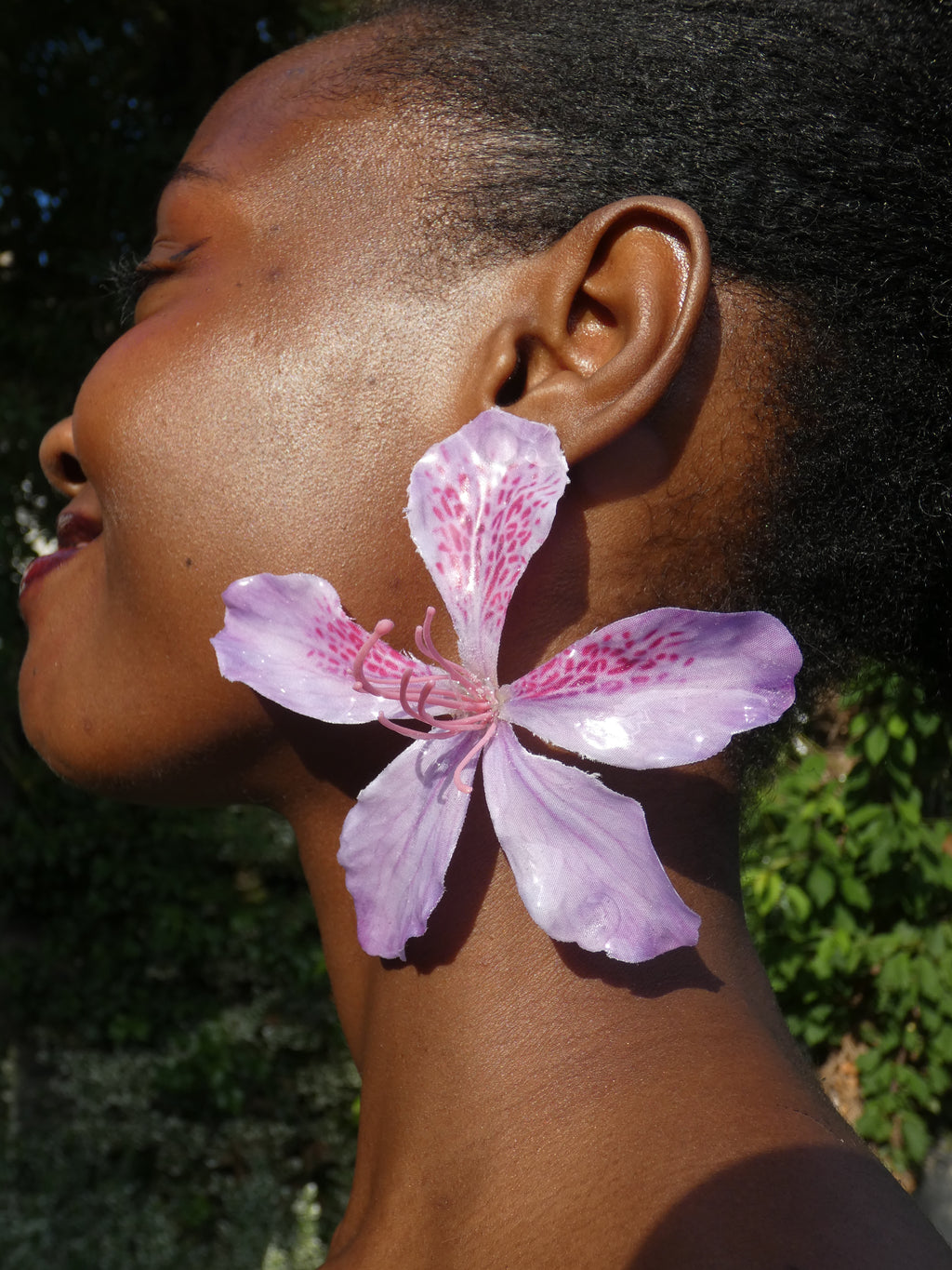 Grande boucle d’oreille fleur rose aux nuances de lilas portée en extérieur