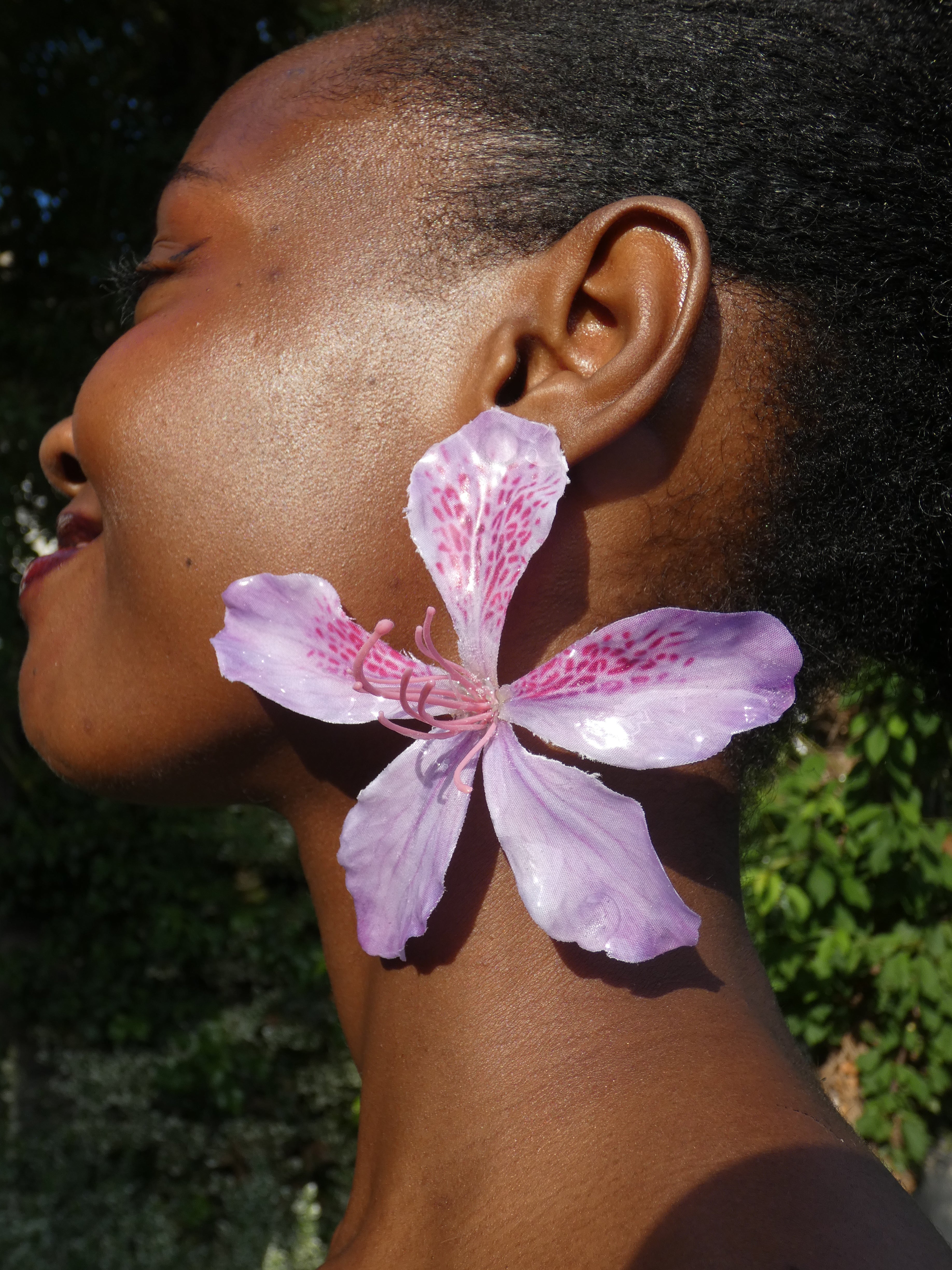 Grande boucle d’oreille fleur rose aux nuances de lilas portée en extérieur