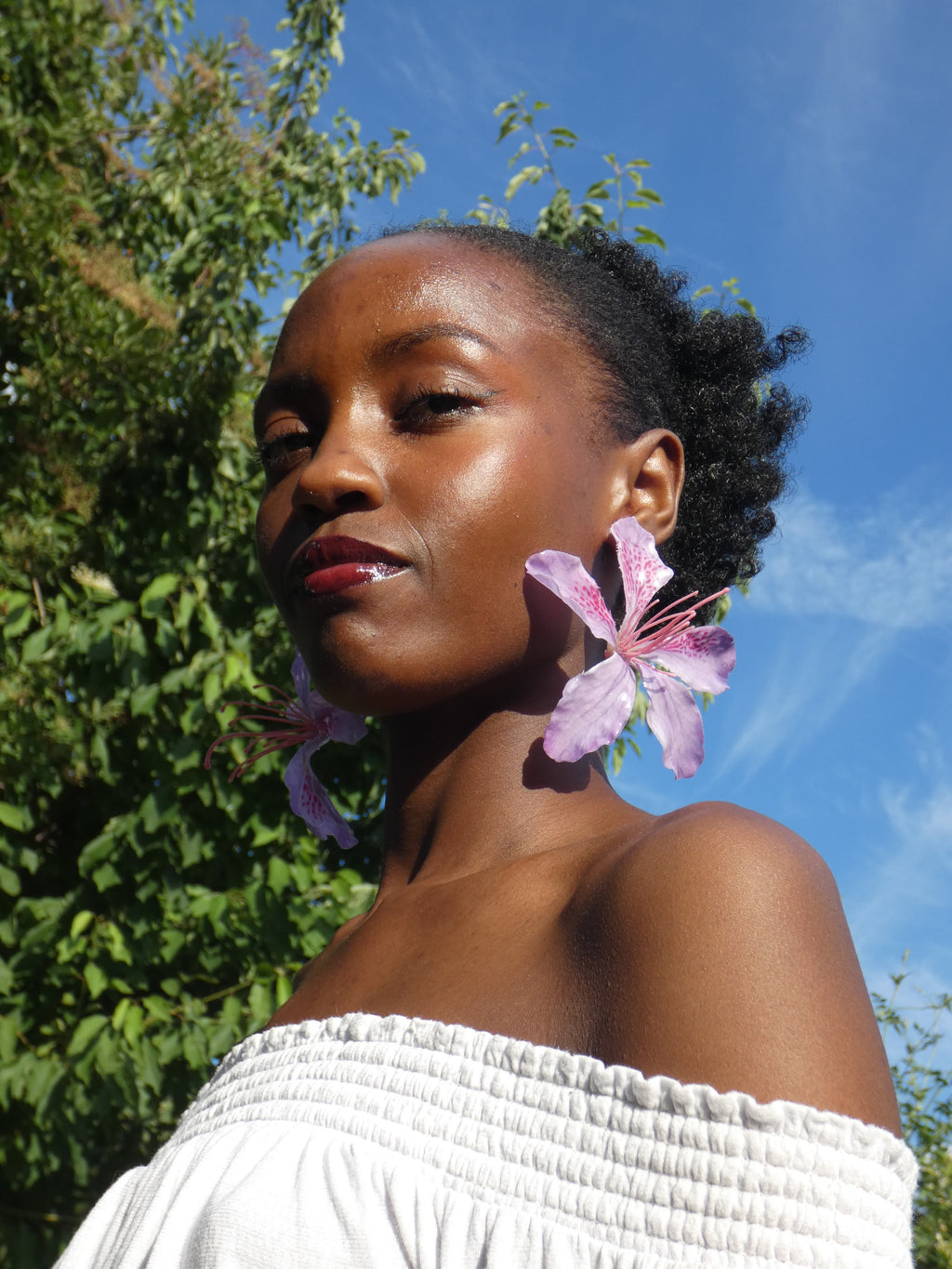 Boucle d’oreille fleur tropicale rose tendre et lilas portée par un modèle