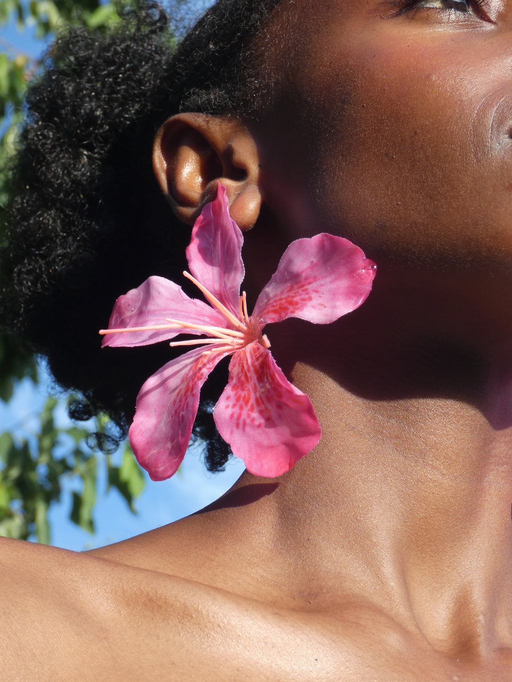 Boucle d’oreille fleur tropicale rose vif artisanale portée à l’oreille
