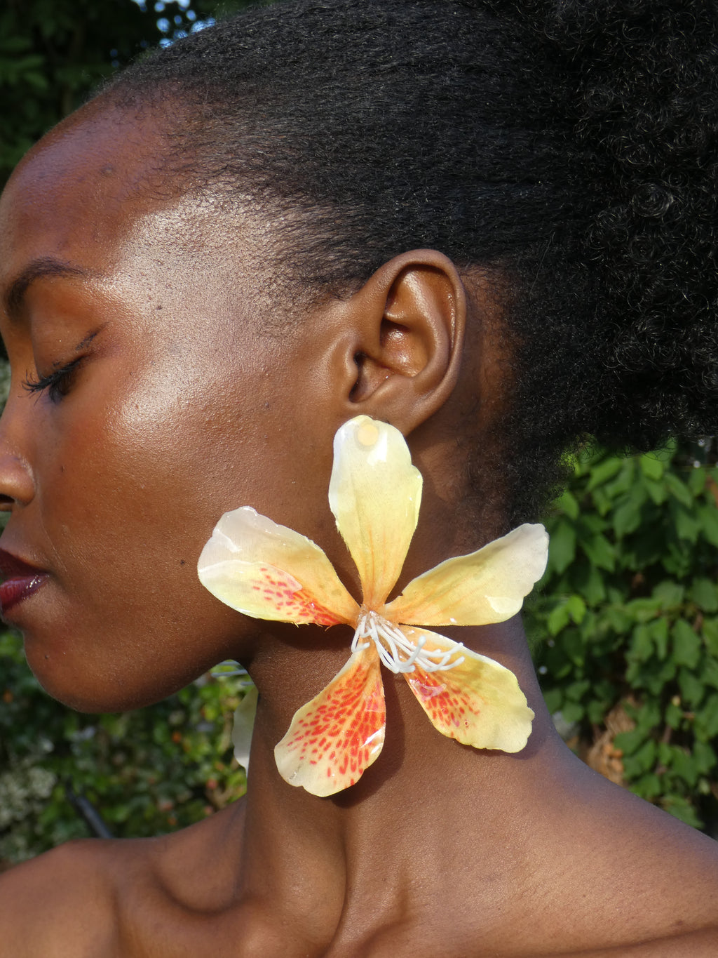 Boucle d'oreille fleur exotique jaune pâle aux détails orange portée à l'oreille