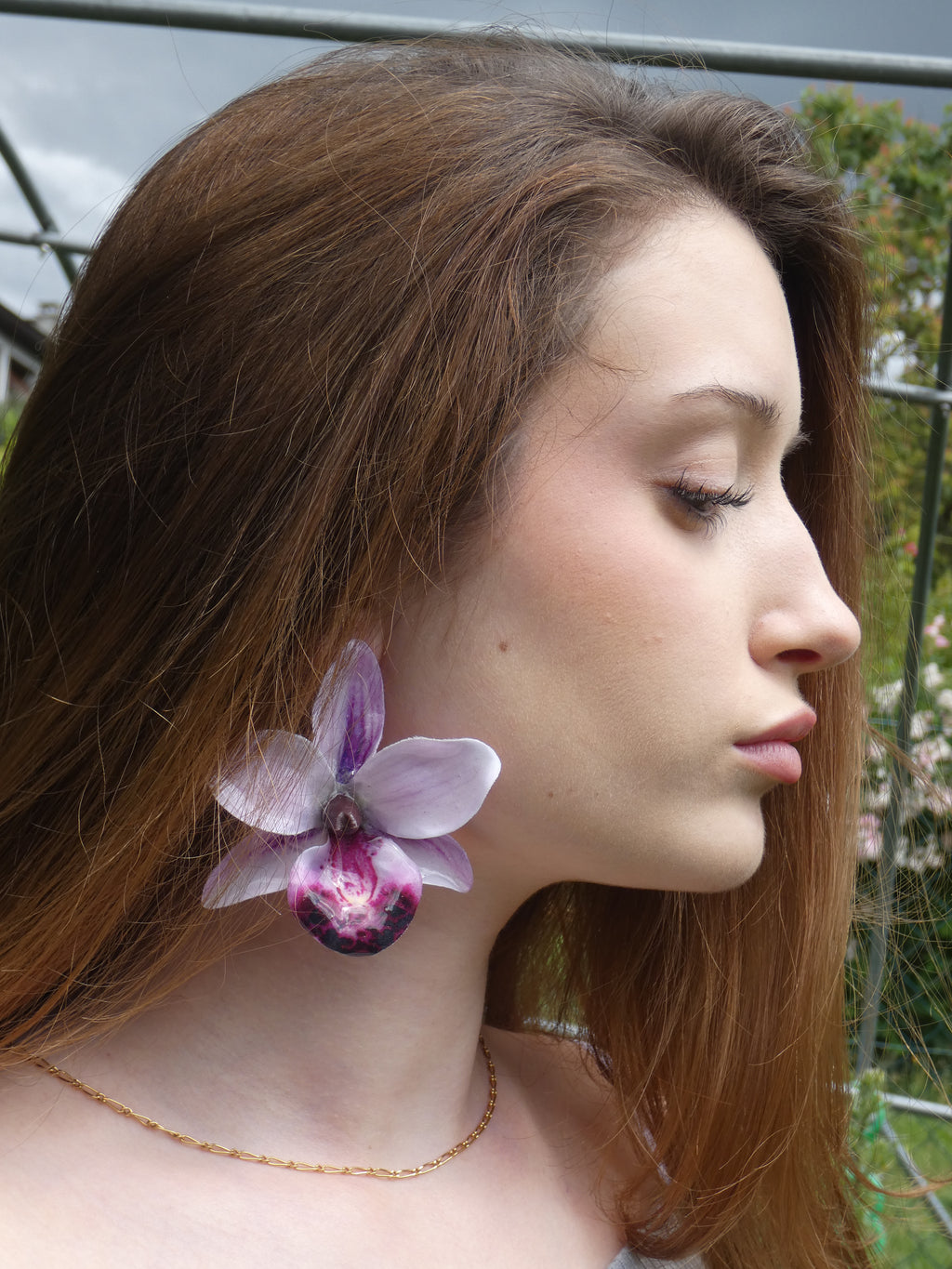Boucle d'oreille orchidée artisanale aux multiples nuances de violet portée à l'oreille
