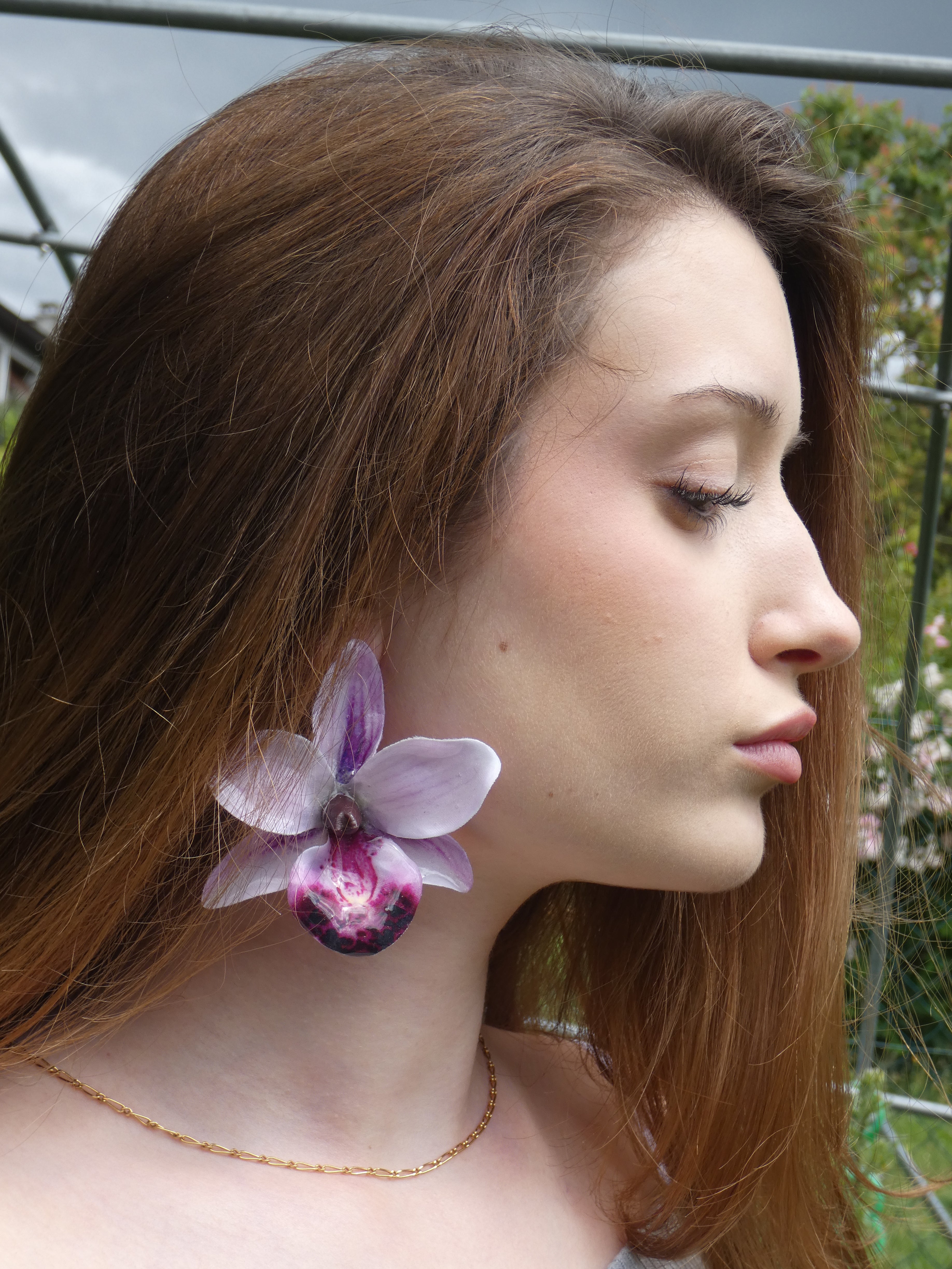 Boucle d'oreille orchidée artisanale aux multiples nuances de violet portée à l'oreille