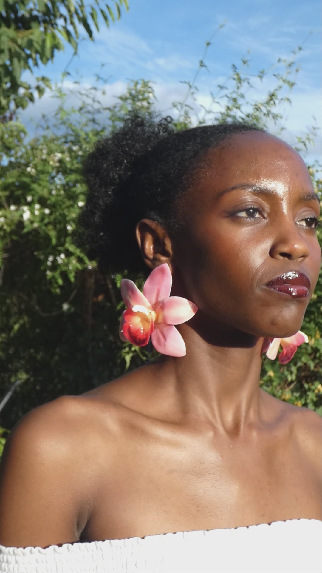 Vidéo montrant le mouvement et les nuances de rose pastel d’une grande boucle d’oreille orchidée artisanale portée par un modèle